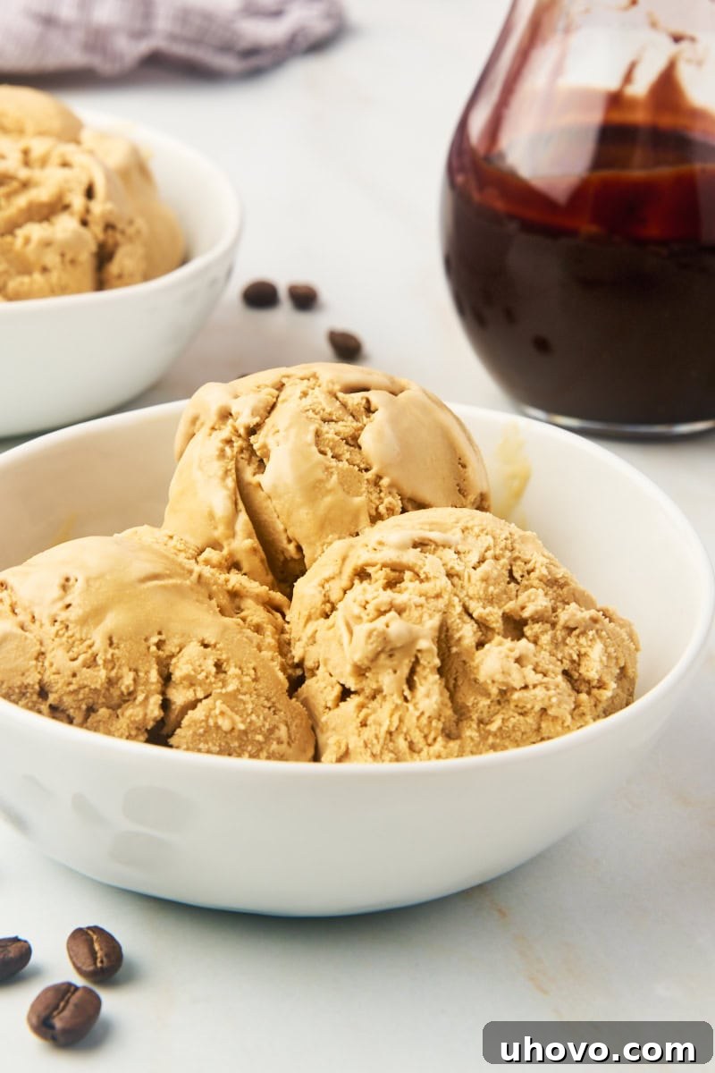 Three scoops of creamy homemade coffee ice cream in a pristine white bowl, garnished with a sprinkle of chocolate shavings.