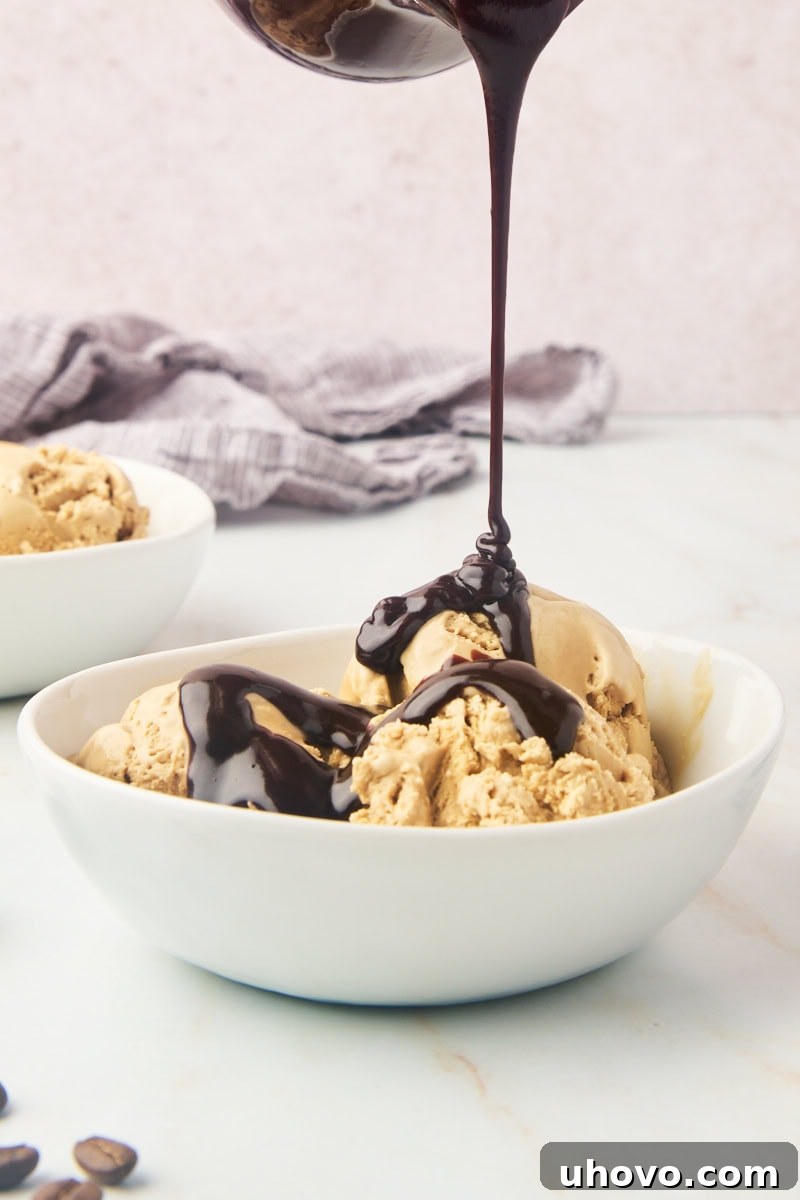A stream of glossy hot fudge sauce drizzling artfully over a scoop of rich coffee ice cream, highlighting its smooth texture and potential for delicious toppings.
