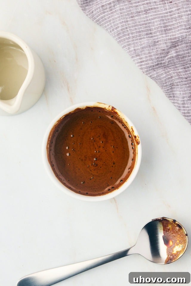Overhead view of rich espresso powder being carefully dissolved in hot water in a clear glass bowl, creating a dark, concentrated coffee liquid.