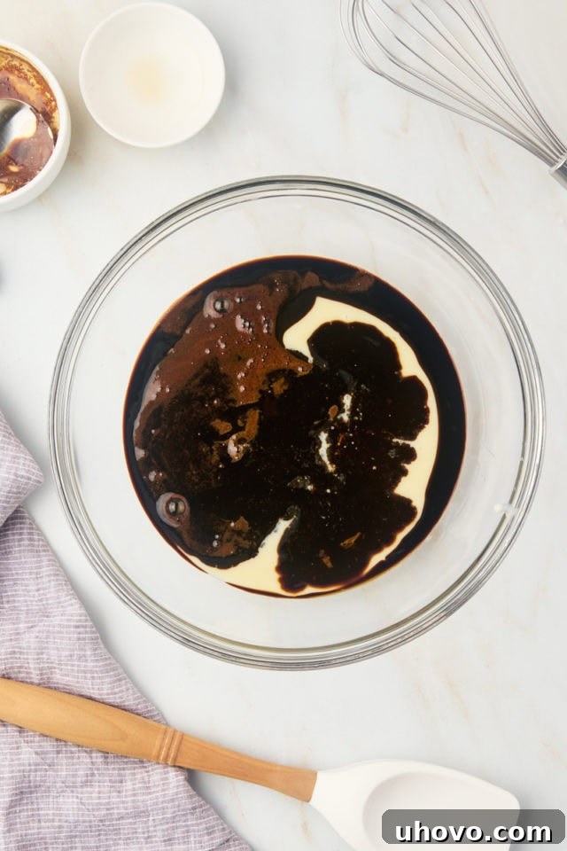 Overhead view of a glass mixing bowl containing creamy condensed milk, dark vanilla extract, and the cooled espresso mixture, ready to be combined.
