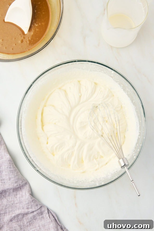 Overhead view of perfectly whipped heavy cream in a clear glass mixing bowl, showcasing soft, glossy stiff peaks.