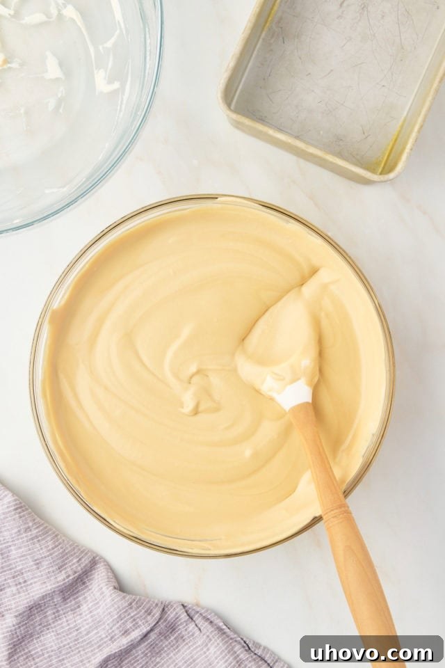 Overhead view of the fully combined, light brown coffee ice cream mixture in a glass mixing bowl, showcasing its smooth and airy consistency after folding.