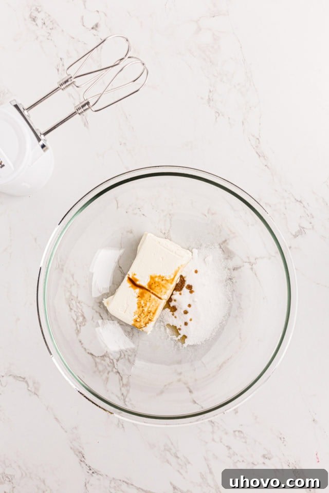 overhead view of cream cheese, sugar, and vanilla extract in a glass mixing bowl