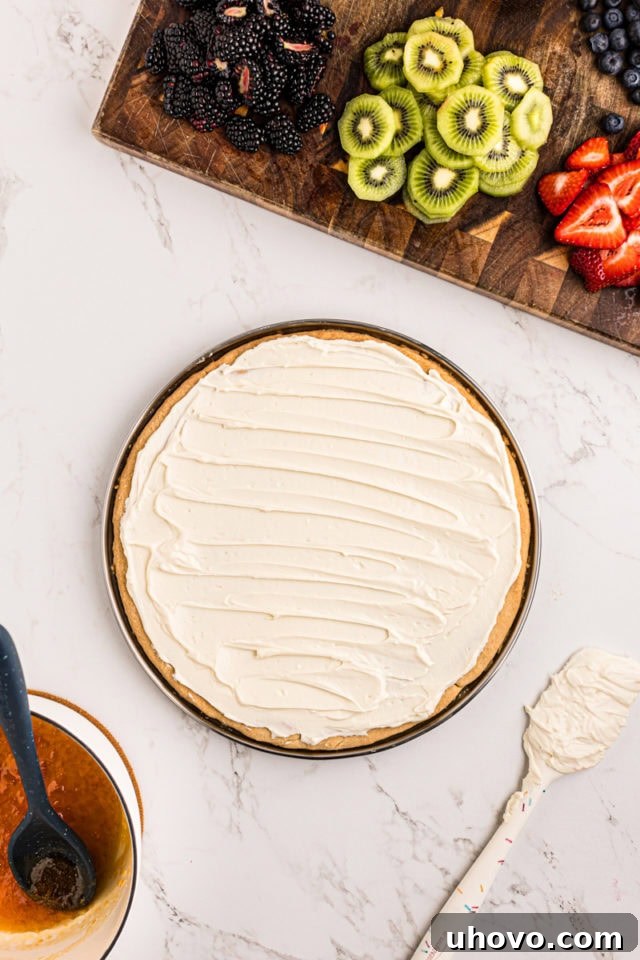 overhead view of cream cheese frosting spread on sugar cookie crust for fruit pizza
