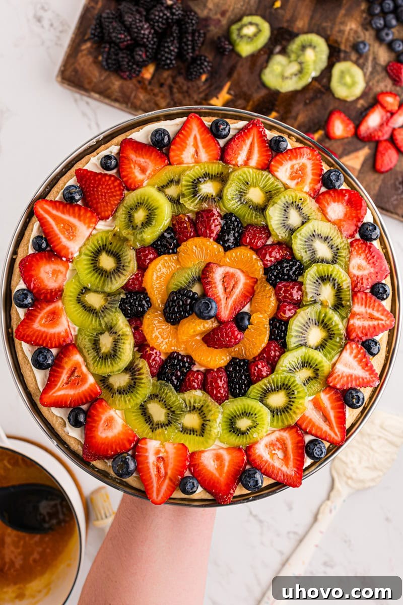 overhead view of fruit pizza being held above a marble countertop