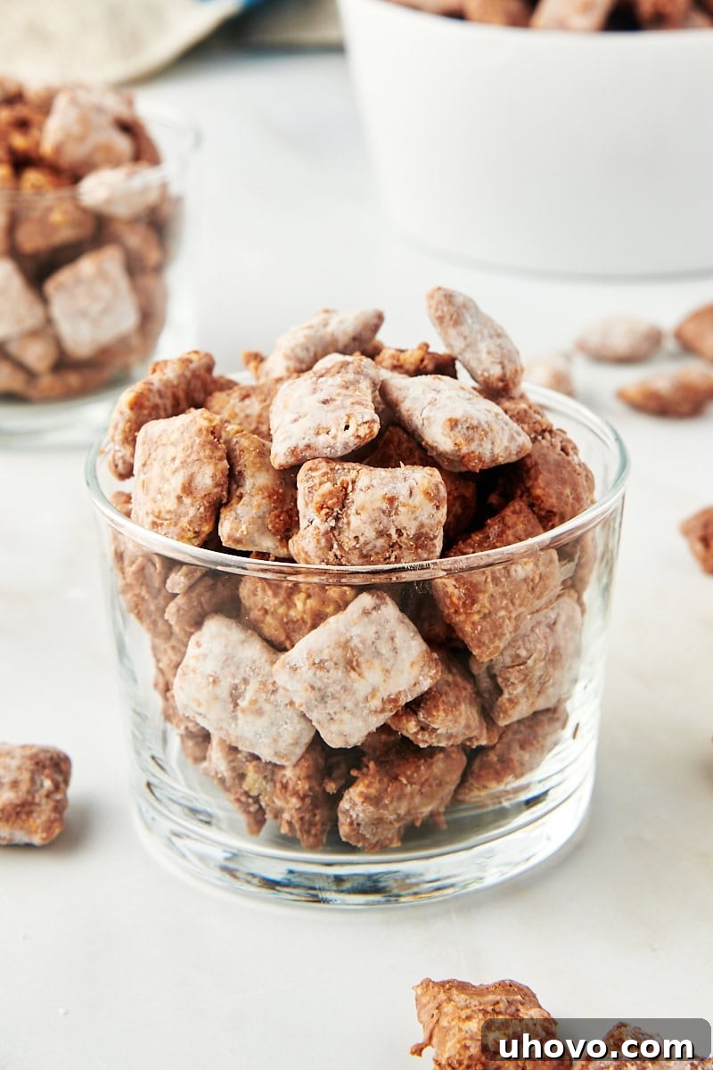 muddy buddies in a small glass with more muddy buddies scattered in the background, showing serving ideas