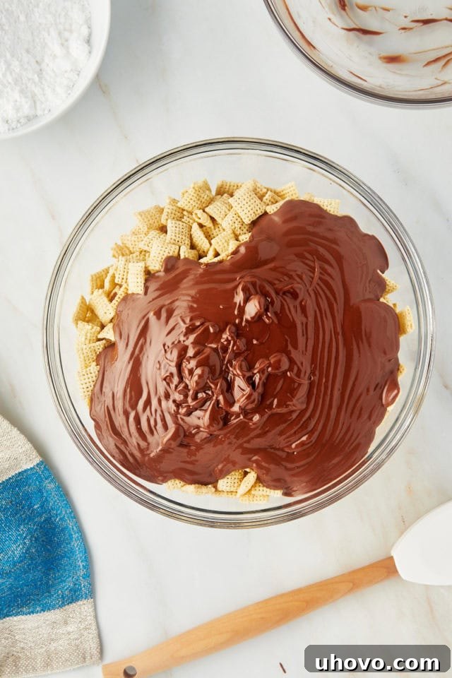 overhead view of the glossy chocolate-peanut butter mixture being poured over crispy rice Chex cereal in a large glass mixing bowl