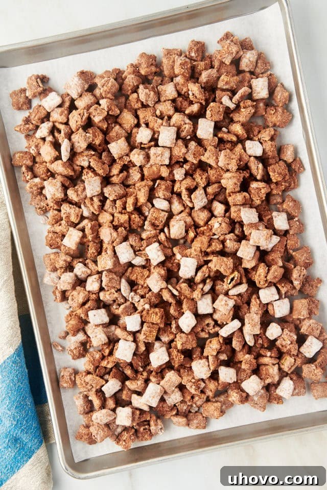 overhead view of muddy buddies spread on a lined baking sheet to cool and set, preventing sticking
