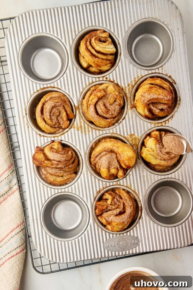 A tempting overhead shot of freshly baked cruffins, still warm from the oven, being generously sprinkled with an additional layer of cinnamon-sugar.