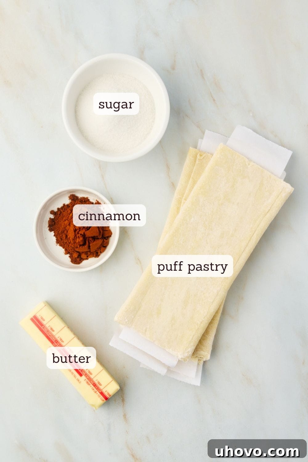 An overhead view of the simple, high-quality ingredients laid out for making cruffins: granulated sugar, ground cinnamon, frozen puff pastry, and softened unsalted butter.
