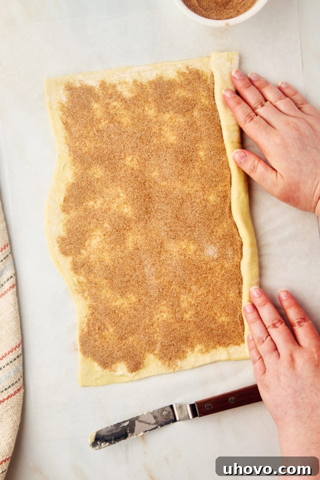 An overhead view demonstrating the process of tightly rolling the puff pastry sheet from its long end into a neat, cylindrical log.
