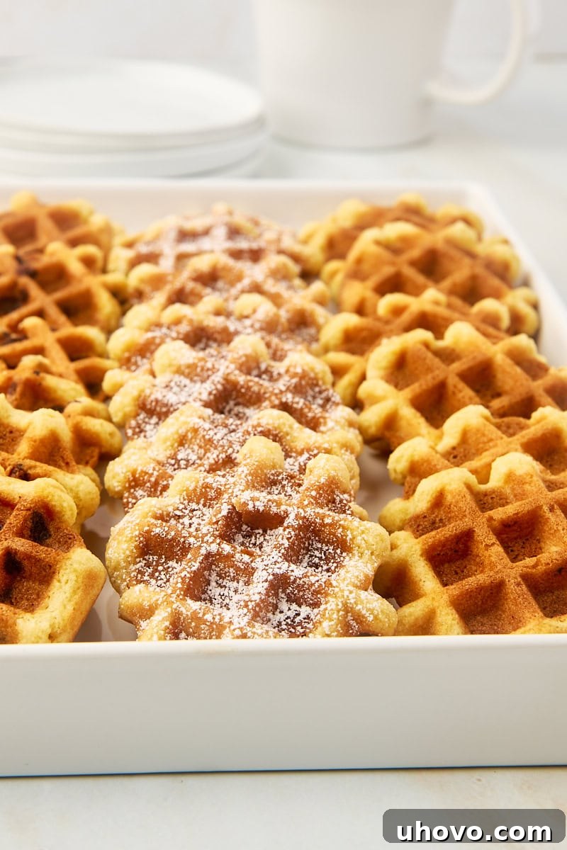 A diverse assortment of waffle cookies, featuring various toppings and mix-ins like chocolate chips, powdered sugar, and glazes, displayed on a pristine white serving tray.