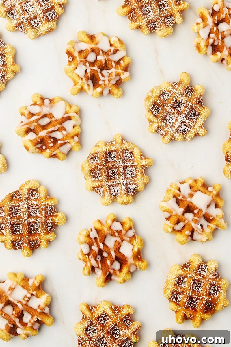 An inviting display of waffle cookies, some elegantly dusted with powdered sugar and others adorned with a delicate glaze, showcasing different topping options on a white surface.