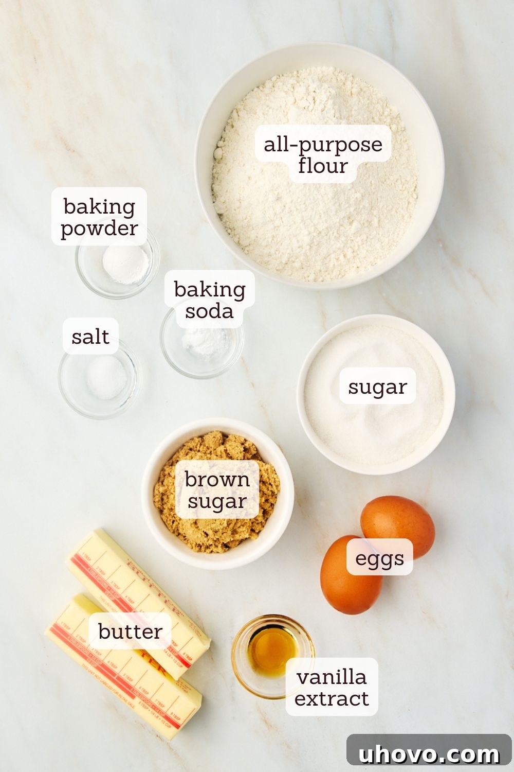 Overhead view of clearly labeled ingredients for making waffle cookies laid out on a clean surface, including flour, sugars, butter, and eggs.