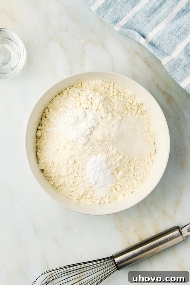 Overhead view of a white mixing bowl containing all-purpose flour, baking powder, baking soda, and salt, perfectly combined for the dry ingredients.