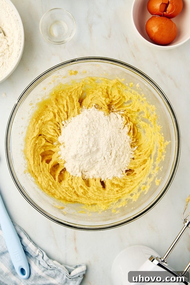 Overhead view as dry ingredients are slowly incorporated into the wet mixture in a mixing bowl, showcasing the careful blending needed for waffle cookie dough.