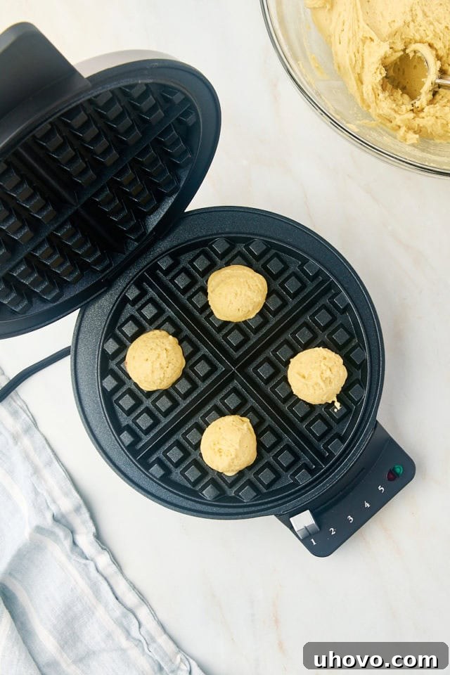 Overhead shot of small scoops of waffle cookie dough neatly placed onto a preheated waffle maker, showing proper spacing for even cooking.