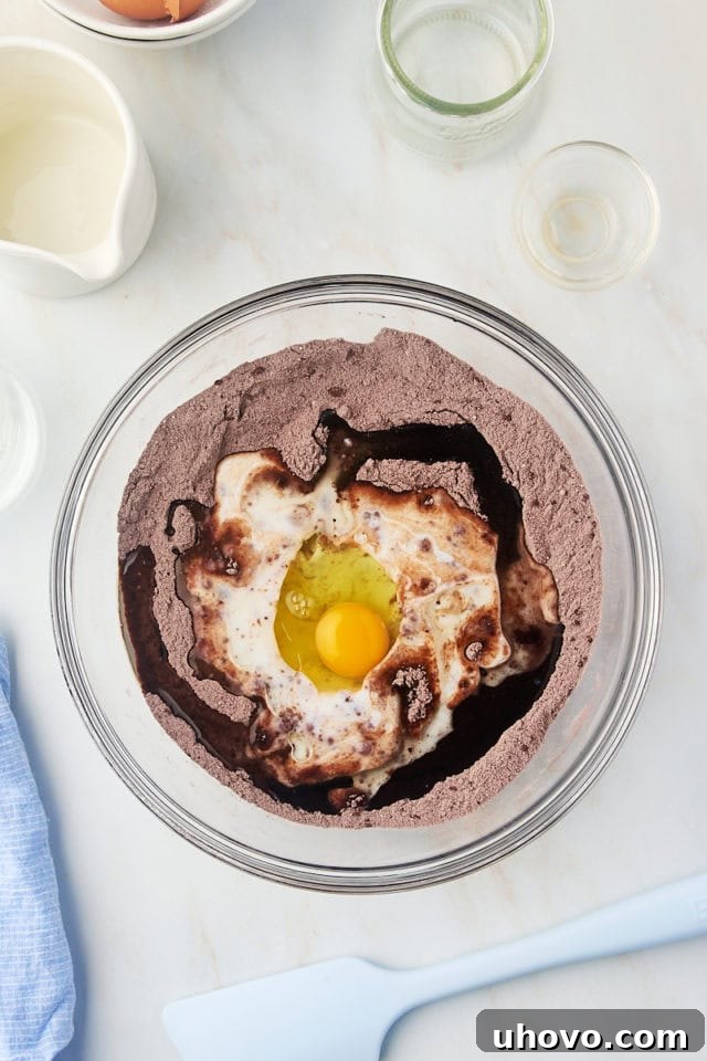 overhead view of egg, buttermilk, oil, and vanilla added to dry ingredients for one-bowl chocolate cake