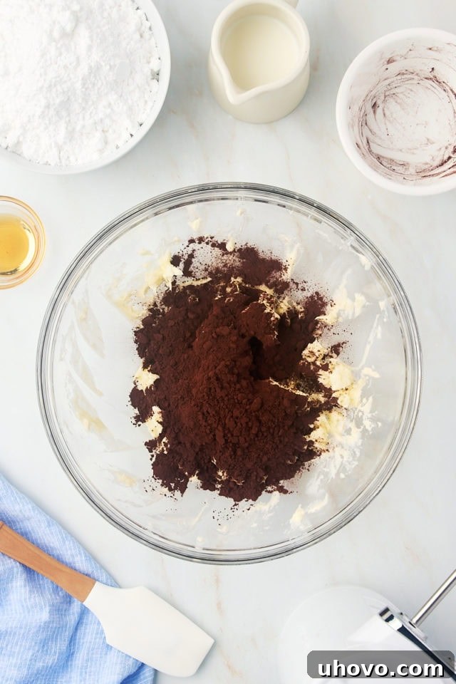 overhead view of cocoa powder added to creamed butter in a glass mixing bowl