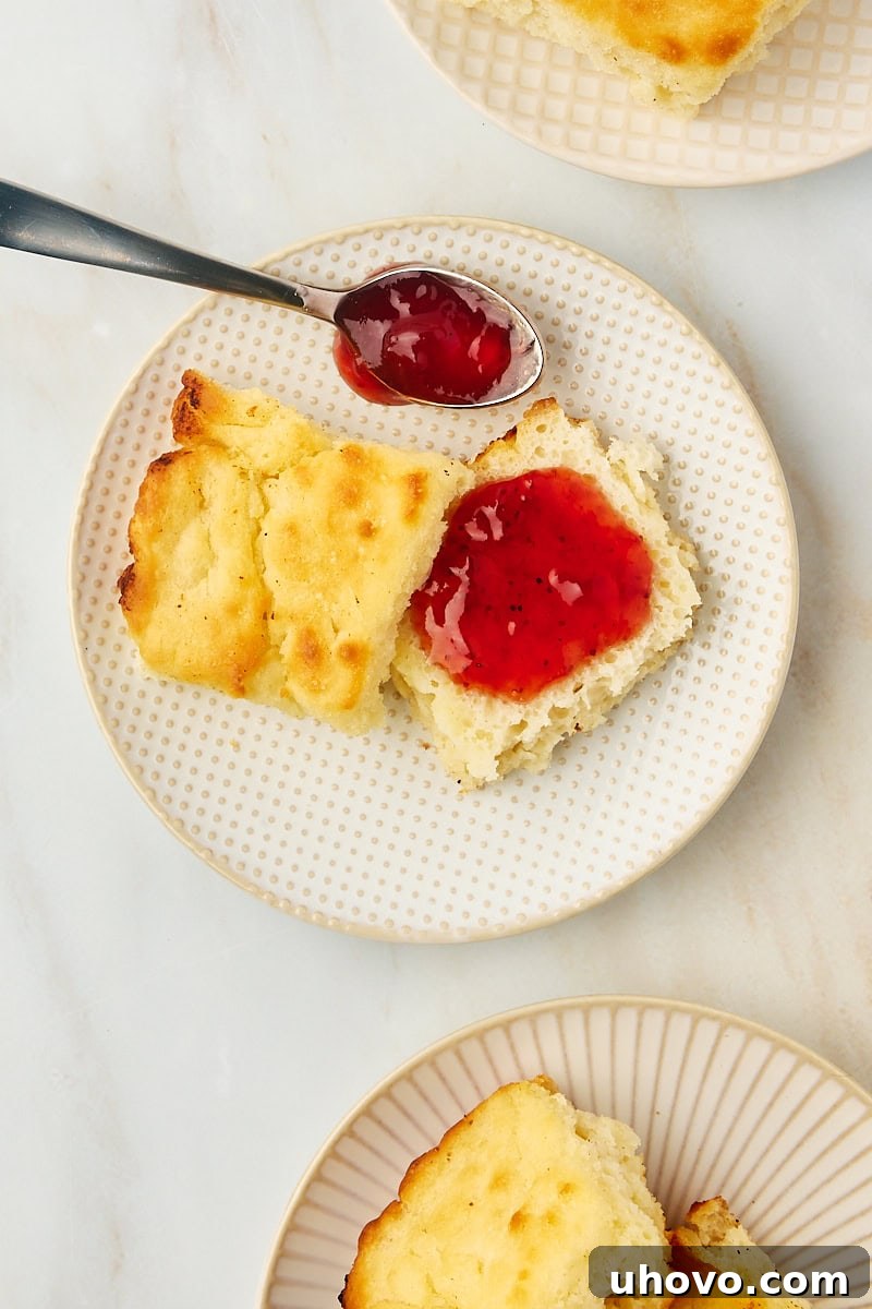 Overhead view of a butter swim biscuit split in half, with strawberry jam generously spread on one side.