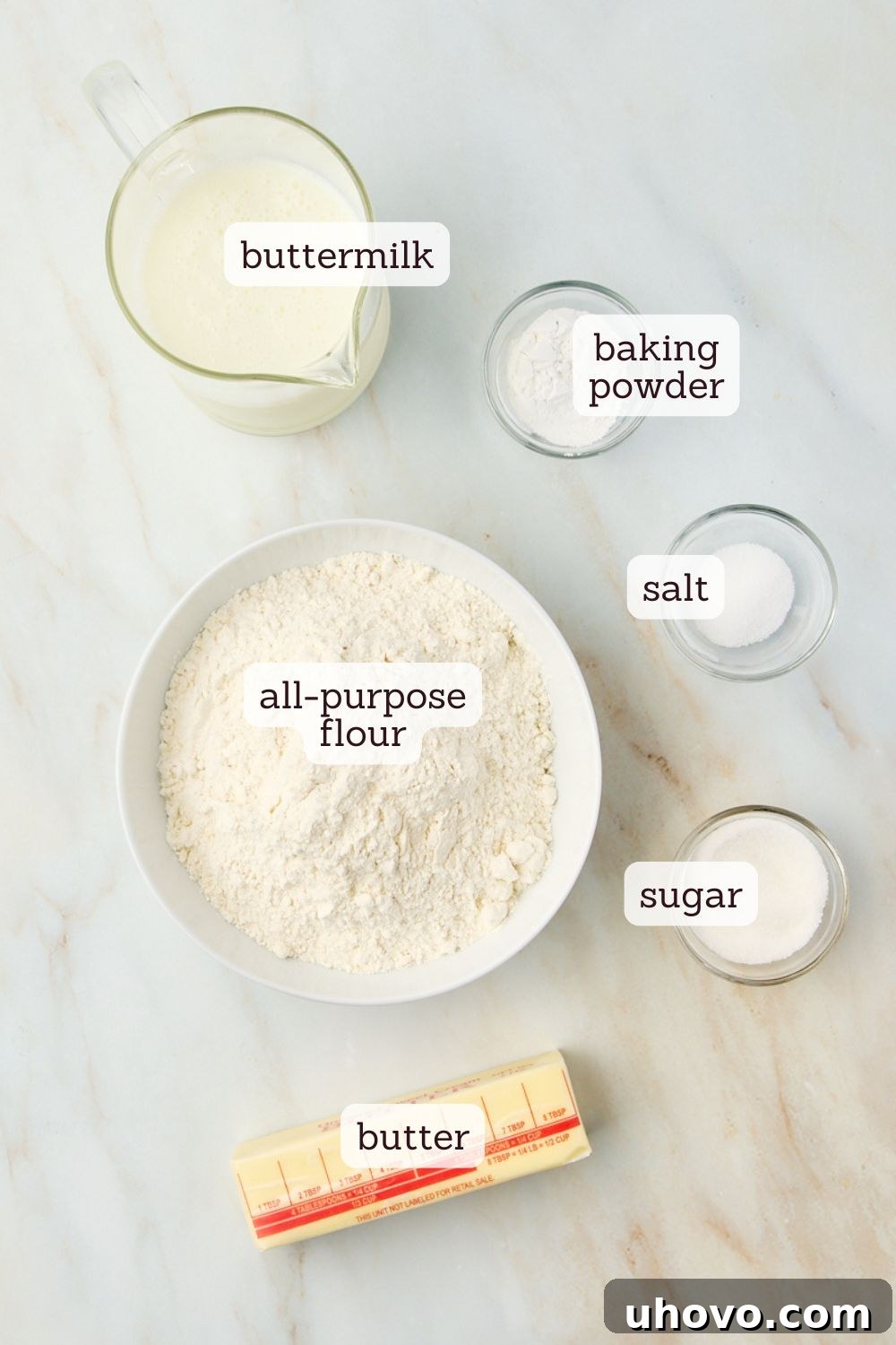Overhead view of labeled ingredients for butter swim biscuits, including flour, baking powder, sugar, salt, buttermilk, and melted butter.