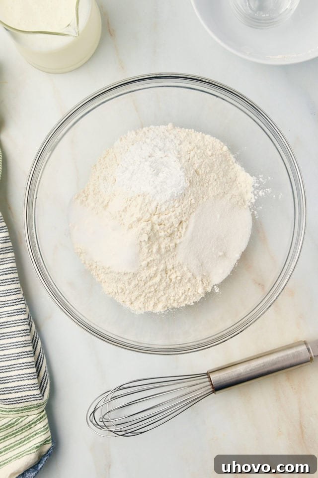 Overhead view of flour, baking powder, sugar, and salt in a glass mixing bowl, ready to be combined.
