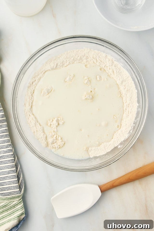 Overhead view of buttermilk being poured into a bowl of dry ingredients for butter swim biscuits.