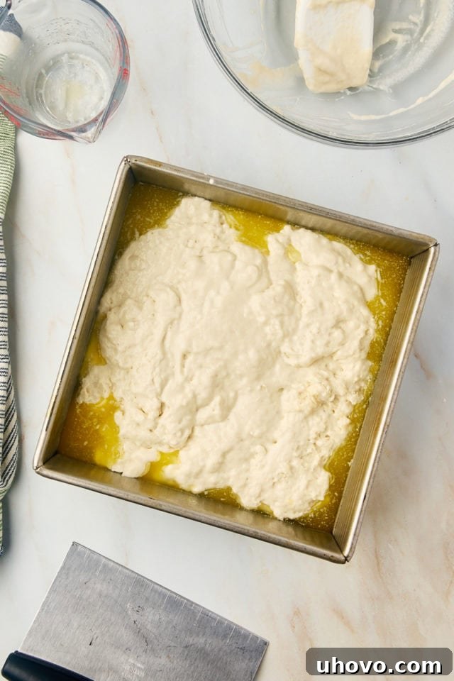 Overhead view of butter swim biscuits dough spread evenly in a baking pan filled with melted butter.