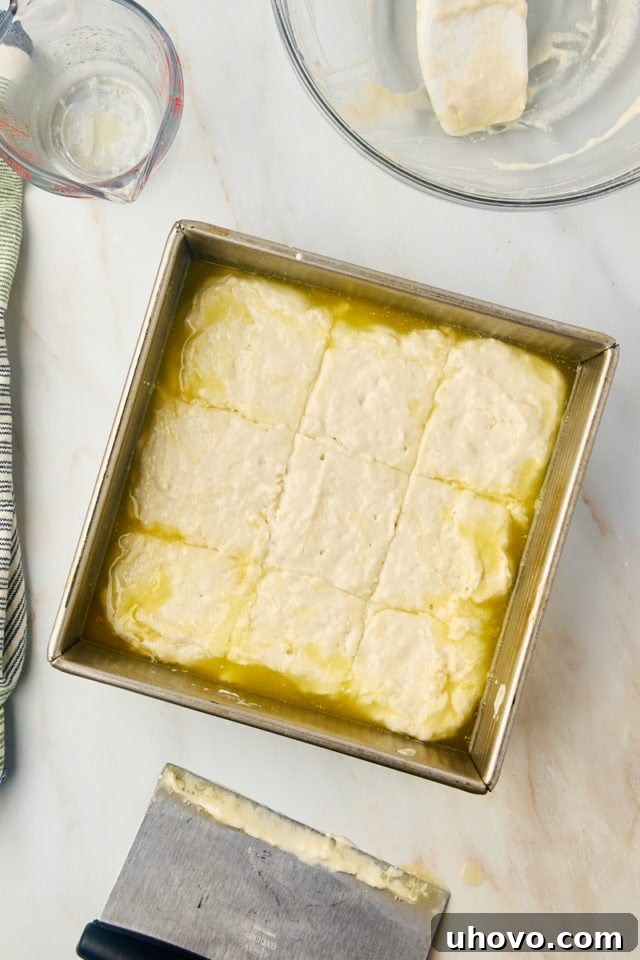 Overhead view of scored butter swim biscuits dough in a metal baking pan, ready for baking.