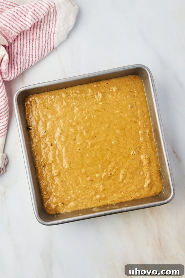 Overhead view of applesauce cake batter spread evenly in an 8-inch square baking pan, ready for the oven.
