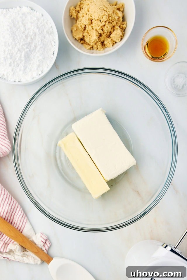 Overhead view of softened cream cheese and butter in a glass mixing bowl, ready to be beaten for frosting.
