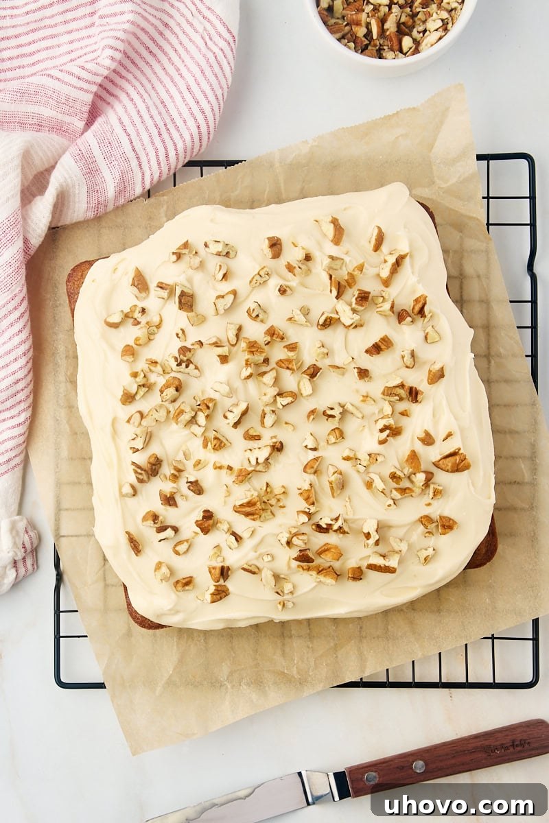 Overhead view of a fully frosted applesauce cake resting on parchment paper on a wire rack, ready for slicing.