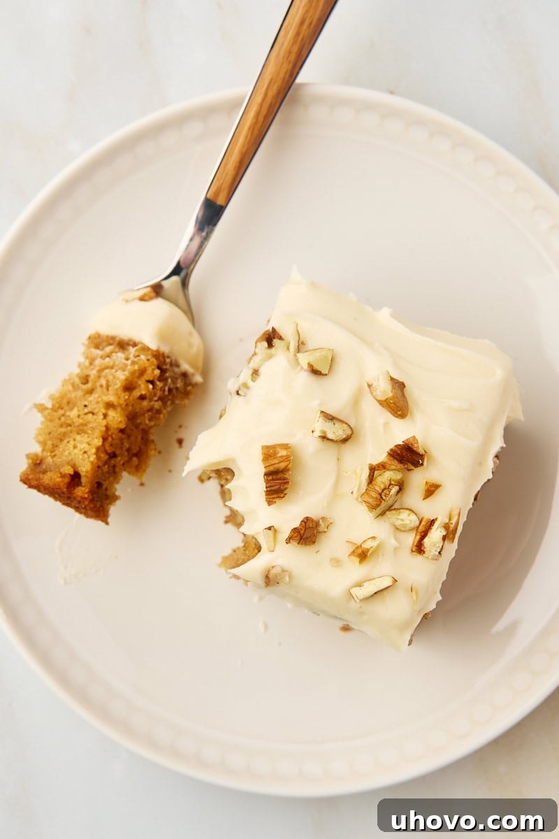 Overhead view of a slice of applesauce cake with a bite taken, resting on a white plate with a fork.