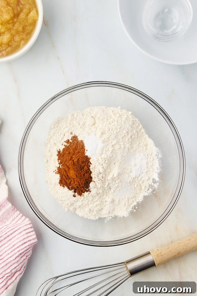 Overhead view of dry ingredients for applesauce cake in a glass mixing bowl, including flour, spices, and leavening agents.