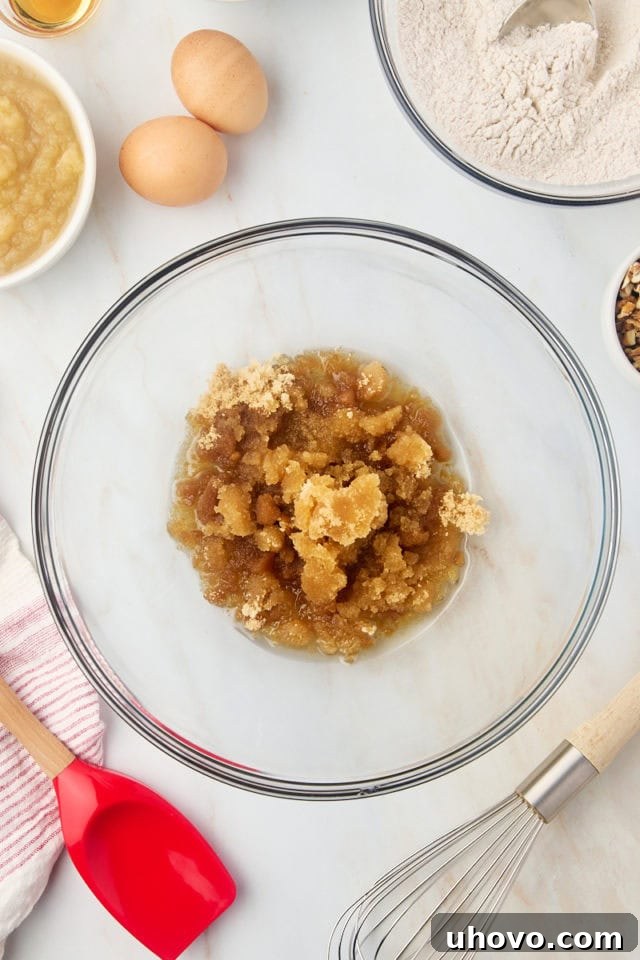 Overhead view of brown sugar and vegetable oil mixed together in a glass mixing bowl, forming a smooth base for the wet ingredients.