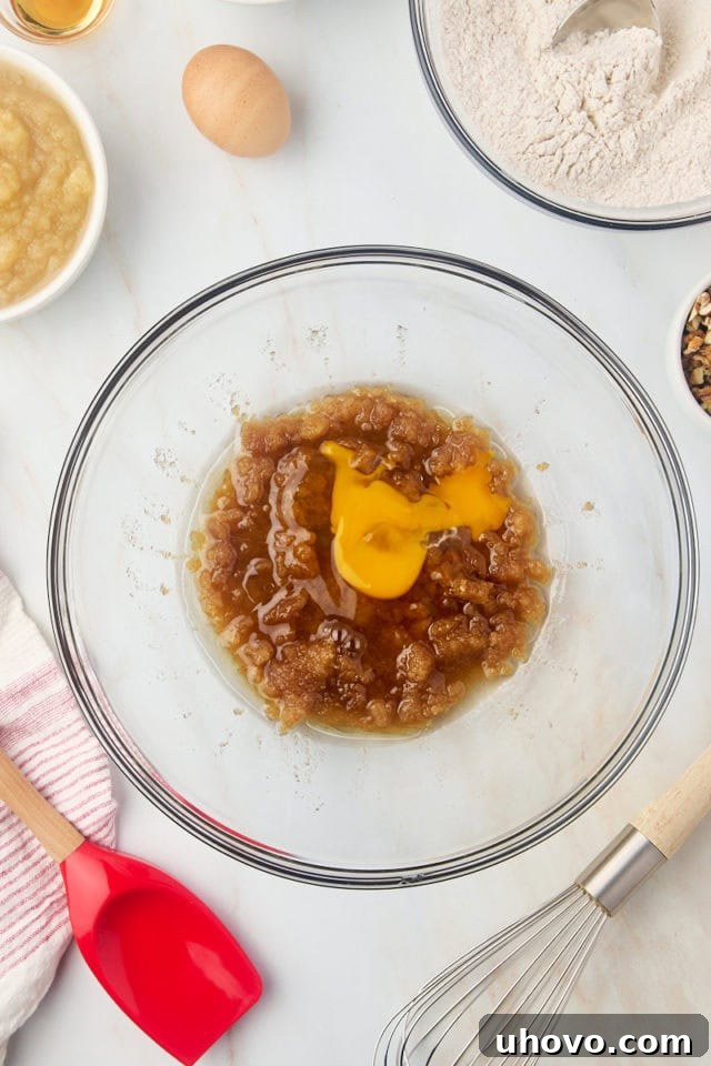 Overhead view of an egg being added to the brown sugar and oil mixture for applesauce cake, ready for whisking.