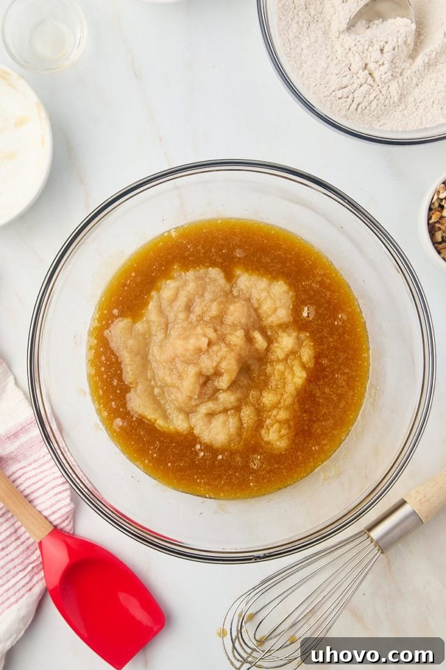 Overhead view of applesauce and vanilla extract being added to the wet ingredients for applesauce cake, ready to be mixed.