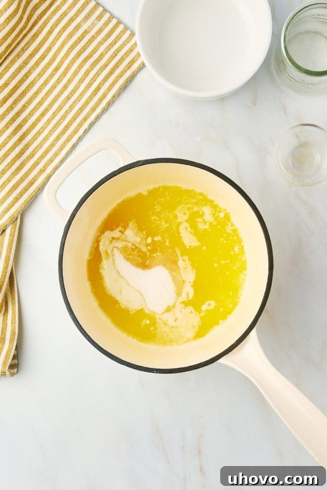 overhead view of sugar, water, and vanilla added to melted butter in a saucepan