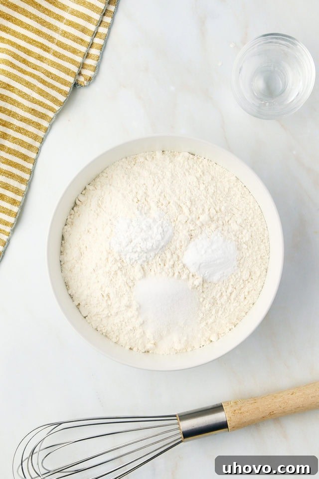 overhead view of flour, baking powder, baking soda, and salt in a glass mixing bowl