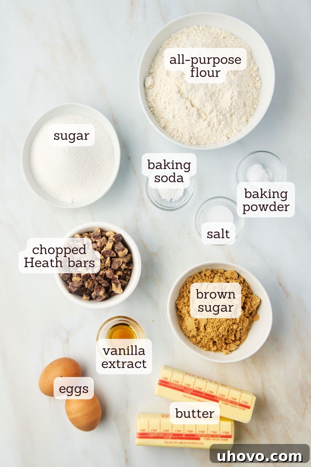 Overhead view of ingredients for Heath bar cookies laid out on a white surface.