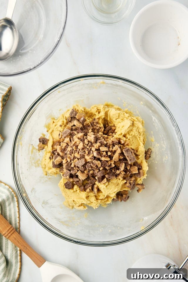Toffee bits being folded into a bowl of cookie dough.