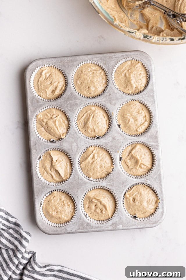Overhead view of chai spice cupcake batter neatly portioned into muffin cups in a muffin pan, ready for baking.