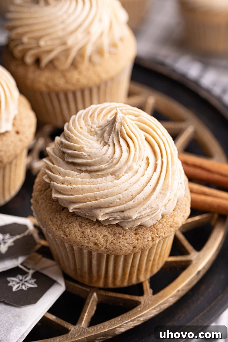 A single, perfectly frosted chai spice cupcake presented on a charming brass and black cake stand.