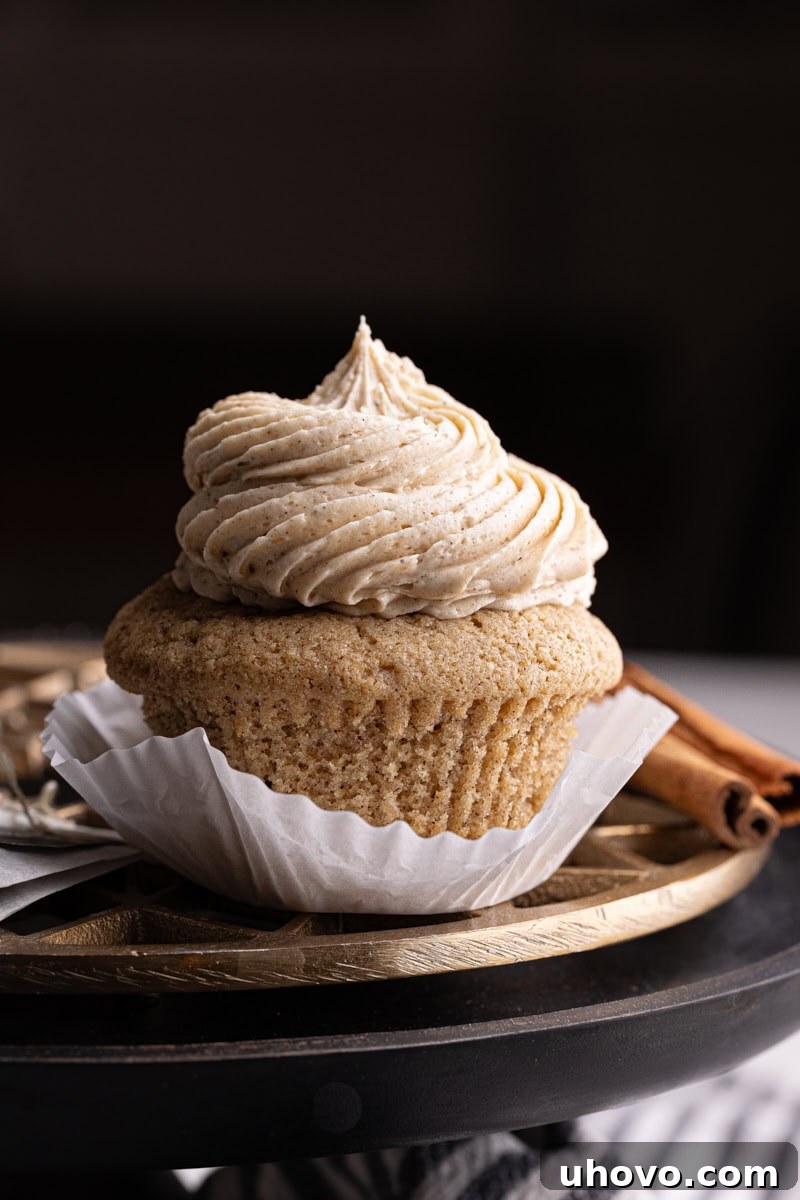 A partially unwrapped chai spice cupcake, showing its moist interior, resting on a brass and black cake stand.