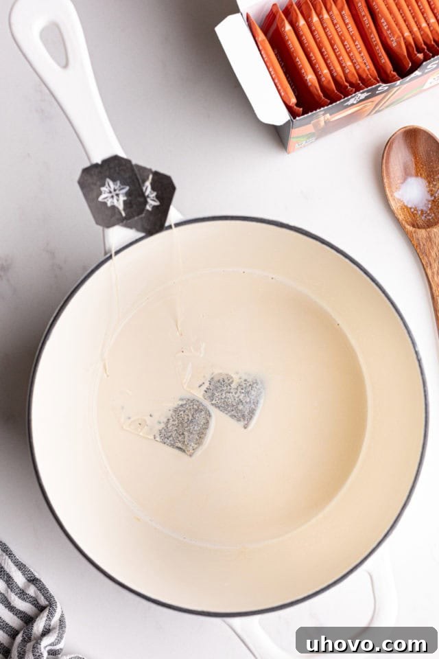 Overhead view of black chai tea bags steeping in warm milk within a saucepan.
