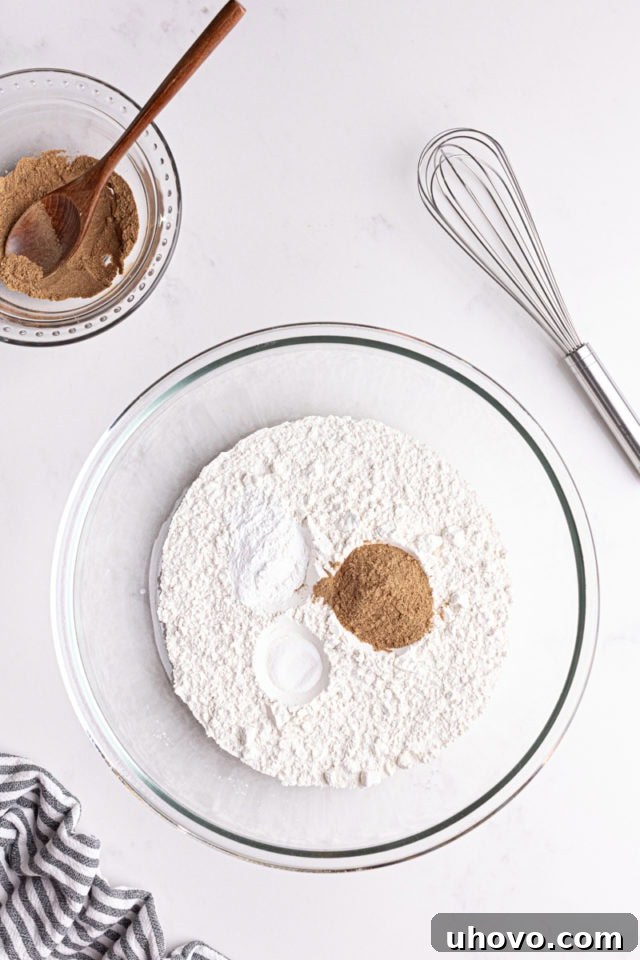 Overhead view of all-purpose flour, baking powder, salt, and chai spices measured into a glass mixing bowl.
