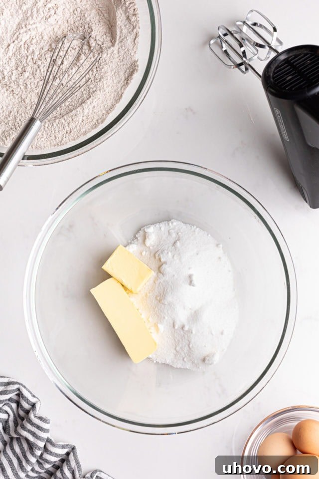 Overhead view of softened unsalted butter and granulated sugar being creamed together in a glass mixing bowl.