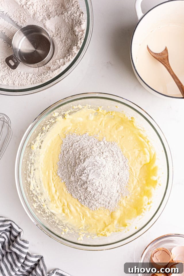 Overhead view of dry ingredients being added to the wet ingredients, alternating with the steeped chai milk mixture, in a glass bowl.