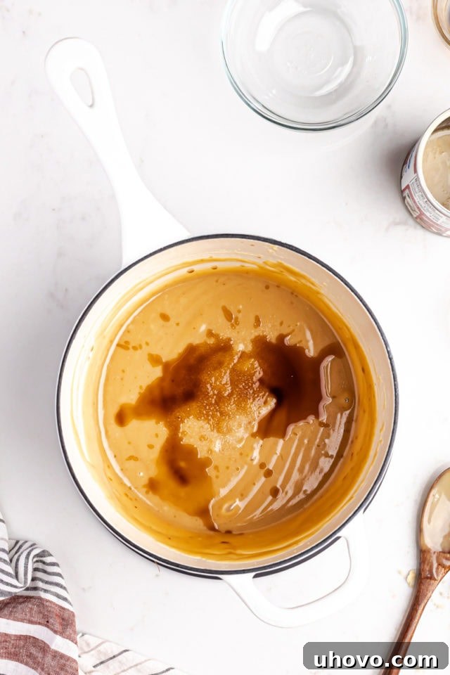 Freshly cooked, thick golden caramel in a saucepan, with vanilla extract and salt being stirred in after reaching the desired temperature.