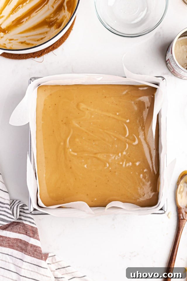 Gooey, golden caramel being spread evenly over the cooled shortbread base in a square pan, creating the second delicious layer.